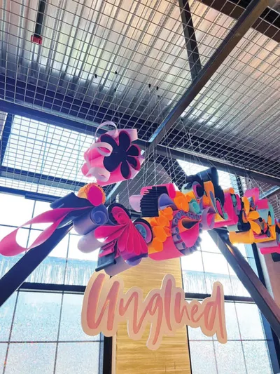 Colorful paper floral installation above a wooden sign reading Unglued