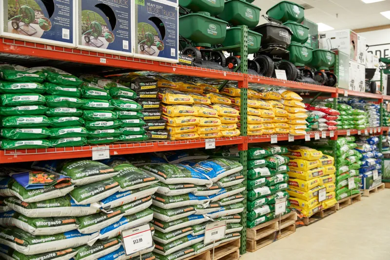Store shelves stocked with colorful lawn fertilizer bags and green spreaders on top