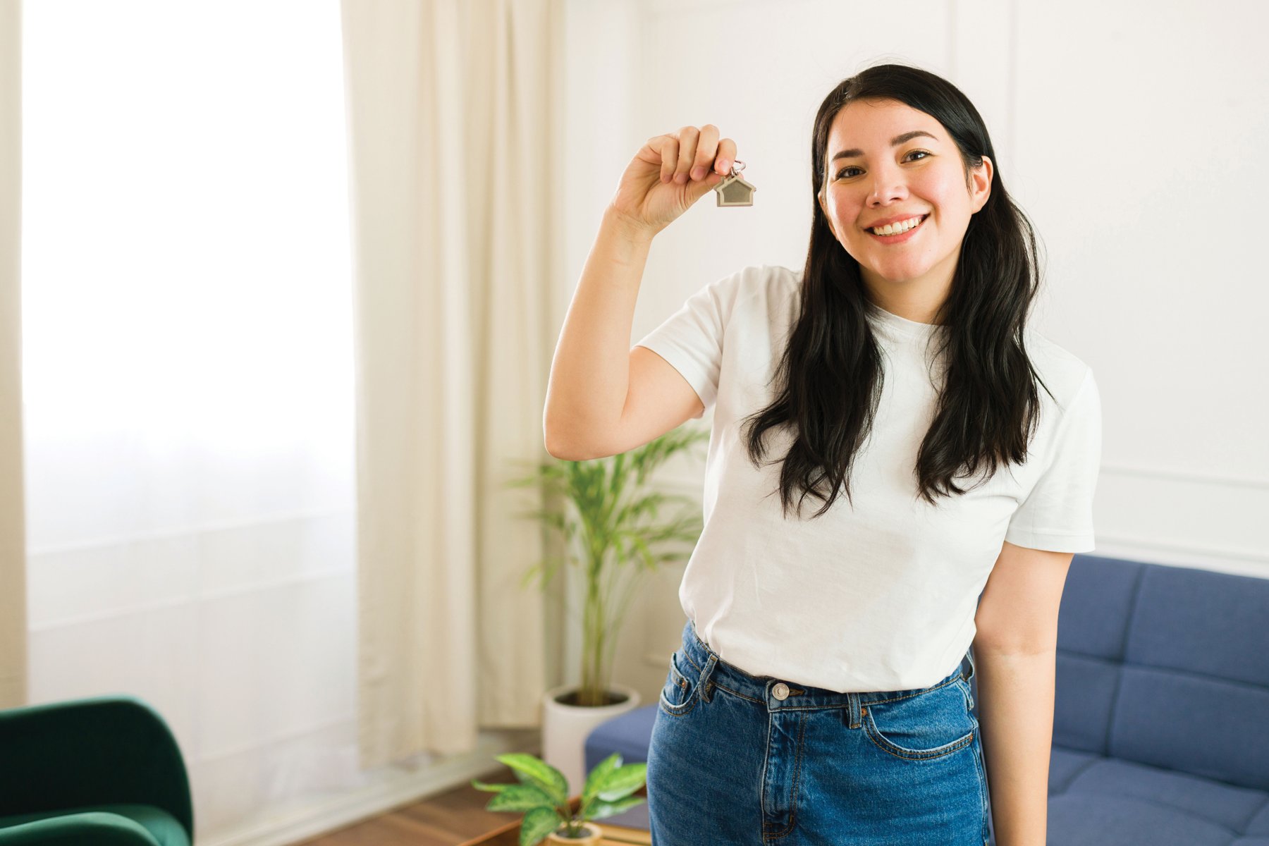 A smiling young woman holds up a house-shaped keychain in her living room