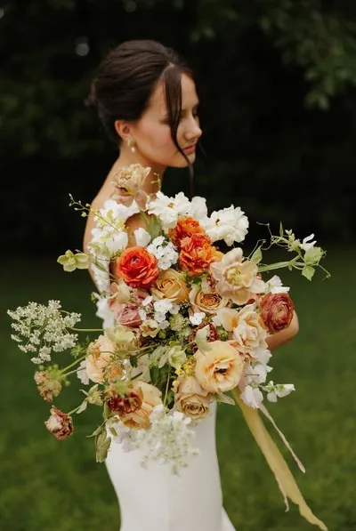 Bride in white gown holding an oversized bouquet of orange, peach, and white blooms