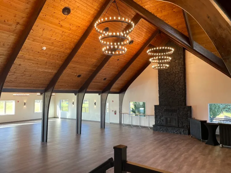 Spacious event hall with vaulted wood ceiling, ring chandeliers, and a dark stone fireplace