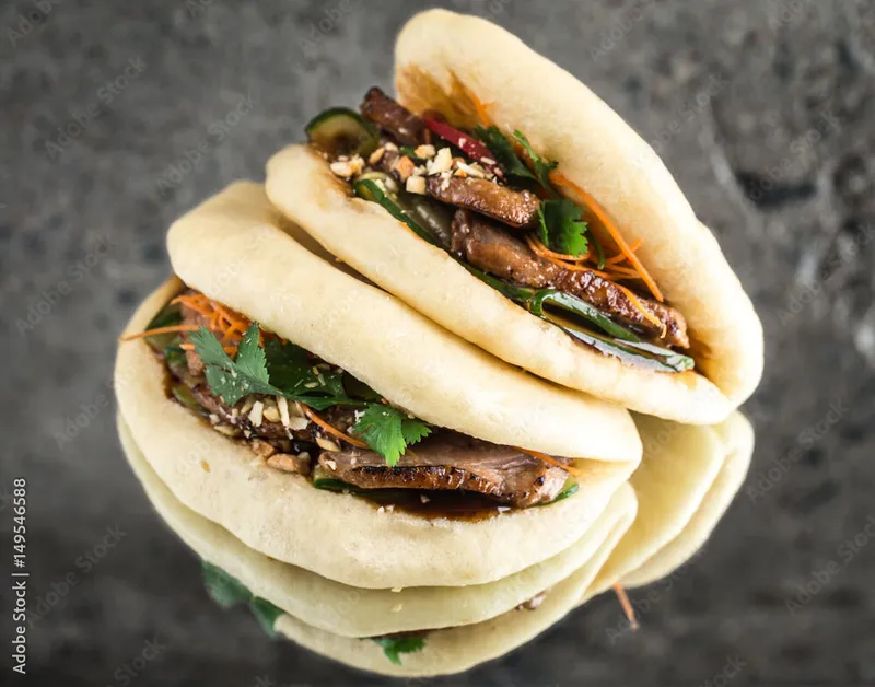 Two steamed bao buns filled with braised meat, cilantro, carrots, and crushed peanuts