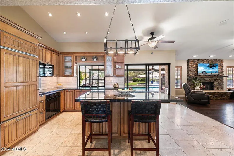 Open-plan kitchen with wood cabinetry, dark granite island, and sliding doors to a backyard pool