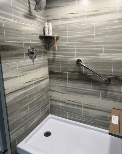 Walk-in shower with gray marble-look tile, chrome grab bar, and white shower base