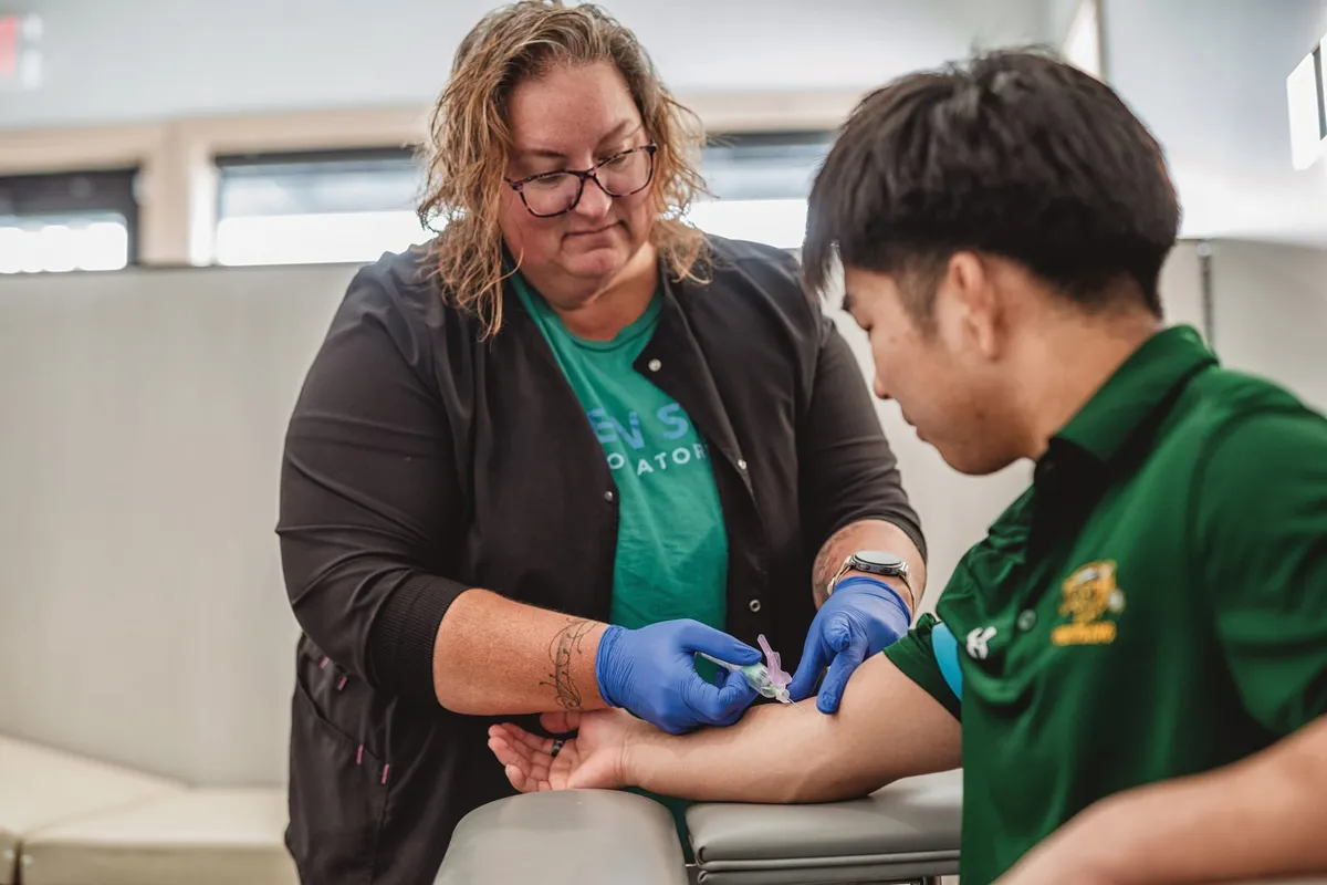 Gloved phlebotomist drawing blood from a young man's arm at a lab clinic