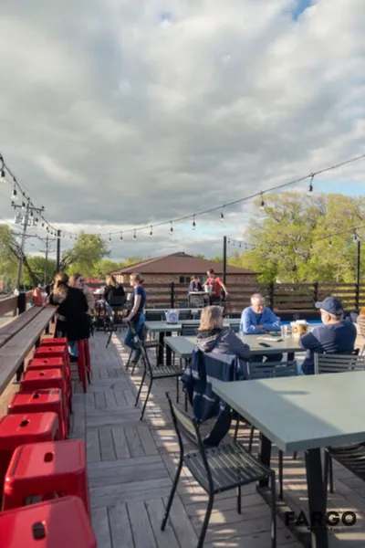 Outdoor restaurant patio with string lights, red stools, and patrons seated at dark metal tables