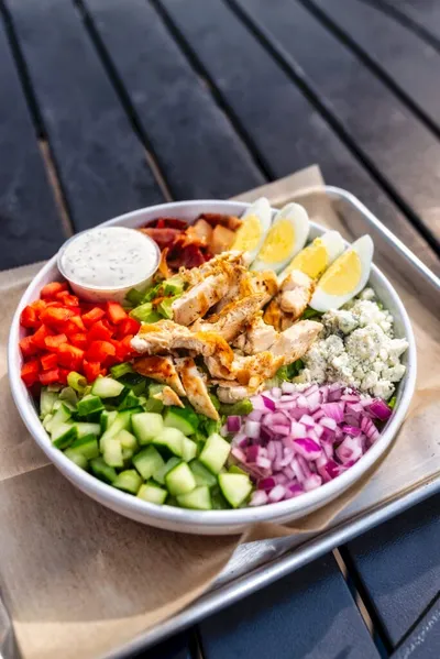 Cobb salad bowl with grilled chicken, halved eggs, red onion, cucumber, red pepper, blue cheese, and ranch dressing