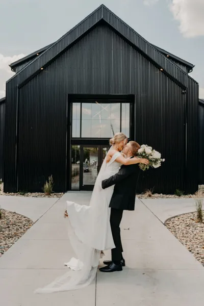 Groom lifting bride in front of a modern black barn-style wedding venue