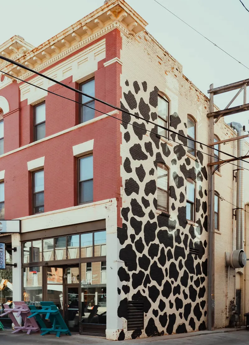 Corner brick building with a bold black-and-white cow-print mural on its side facade