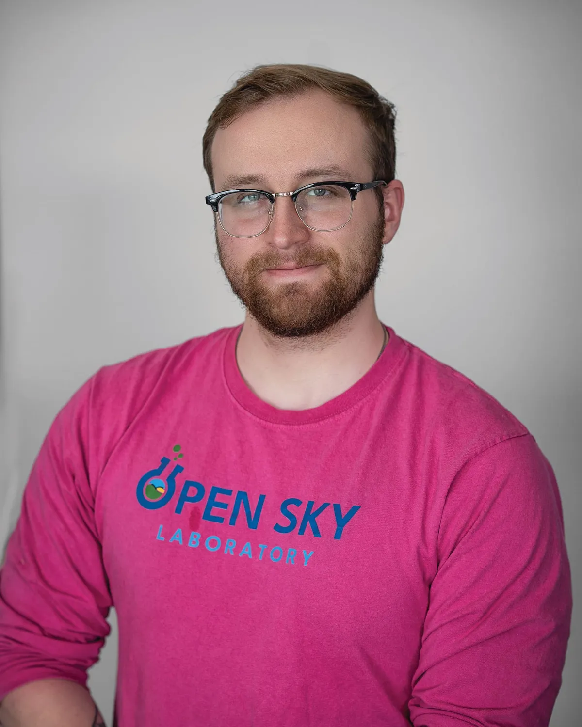 Bearded man with glasses wearing a pink Open Sky Laboratory long-sleeve shirt