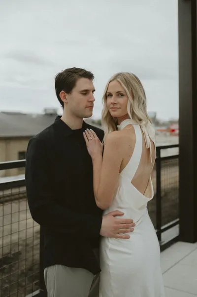 Couple embracing on a rooftop balcony, woman in backless white dress with bow, man in black sweater