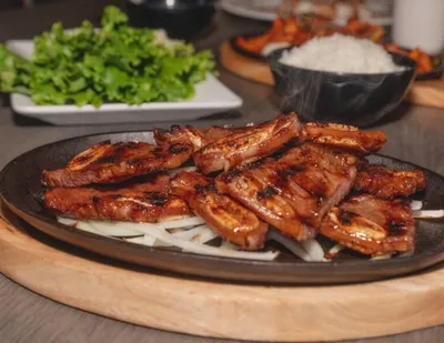 Glazed grilled meat slices on a sizzling cast iron plate with onions, rice and greens in background