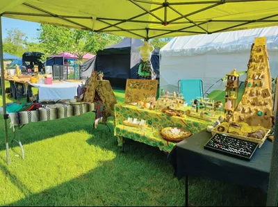 Outdoor craft vendor booth under a yellow canopy displaying handmade stone pieces on draped tables