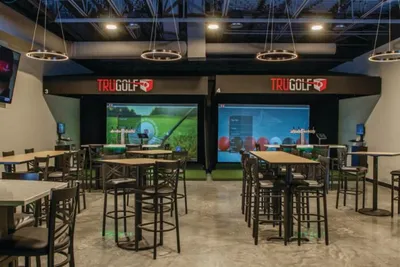 TruGolf indoor simulator venue with high-top tables and large screen displays