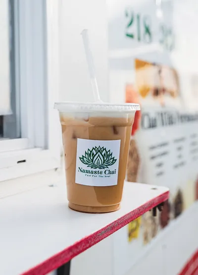 Iced chai latte in a clear plastic cup with a Namaste Chai logo sticker and white straw
