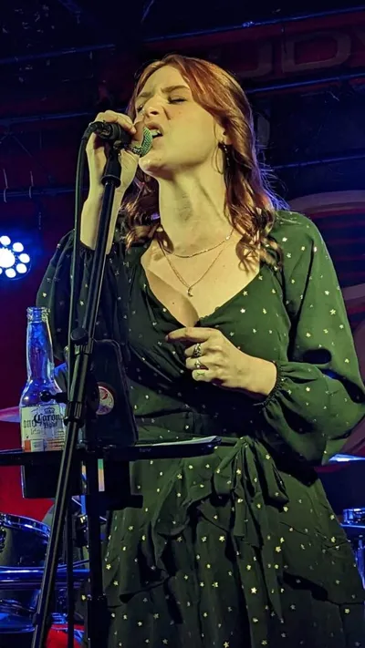 Red-haired woman in a green star-print dress singing into a mic on a dimly lit stage
