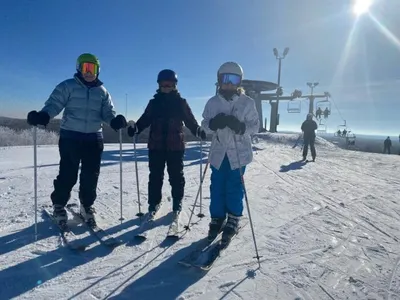 Three skiers in helmets and goggles posing on a sunny snow-covered ski hill with a chairlift behind them