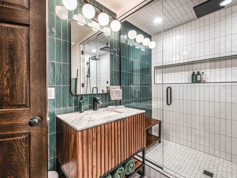 Modern bathroom with teal tile walls, wood vanity, marble countertop, and glass walk-in shower