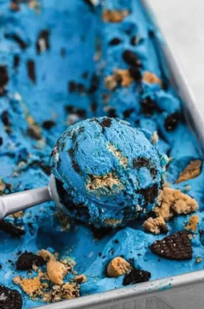A metal scoop lifting a blue ice cream ball with cookie crumbles from a tray