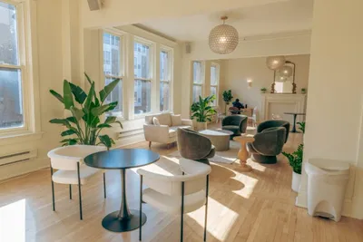 Bright co-working lounge with round café table, cushioned chairs, and tropical plants near tall windows