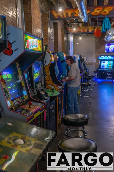 Man playing a classic arcade cabinet in a brick-walled retro arcade bar