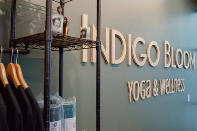 Indigo Bloom Yoga & Wellness sign on a teal wall beside a clothing rack