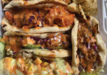 Two saucy tacos with corn and toppings in a takeout container