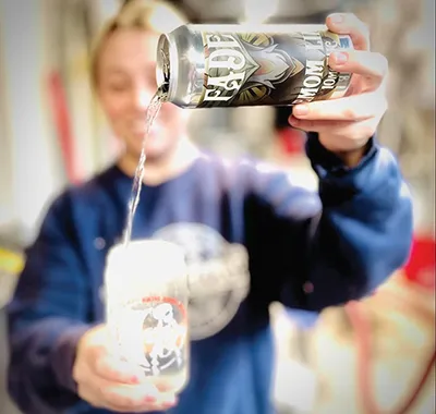 Woman in blue sweatshirt pouring a THC seltzer can into a glass