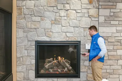 Man in blue vest using a remote control beside a stone fireplace