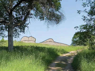 Dirt path leading toward a large reclining figure sculpture made of stone on a grassy hill