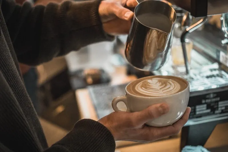Barista pouring steamed milk into a latte with a leaf foam art design