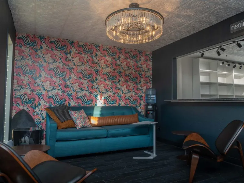 Teal sofa with colorful pillows against bold flamingo wallpaper beneath a crystal chandelier