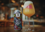 Tall craft beer can beside a hazy golden pint glass on a dark bar top