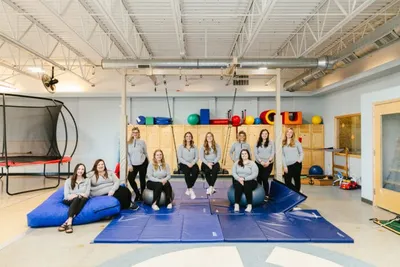 Group of therapists posing in a pediatric gym with mats, exercise balls, and a trampoline