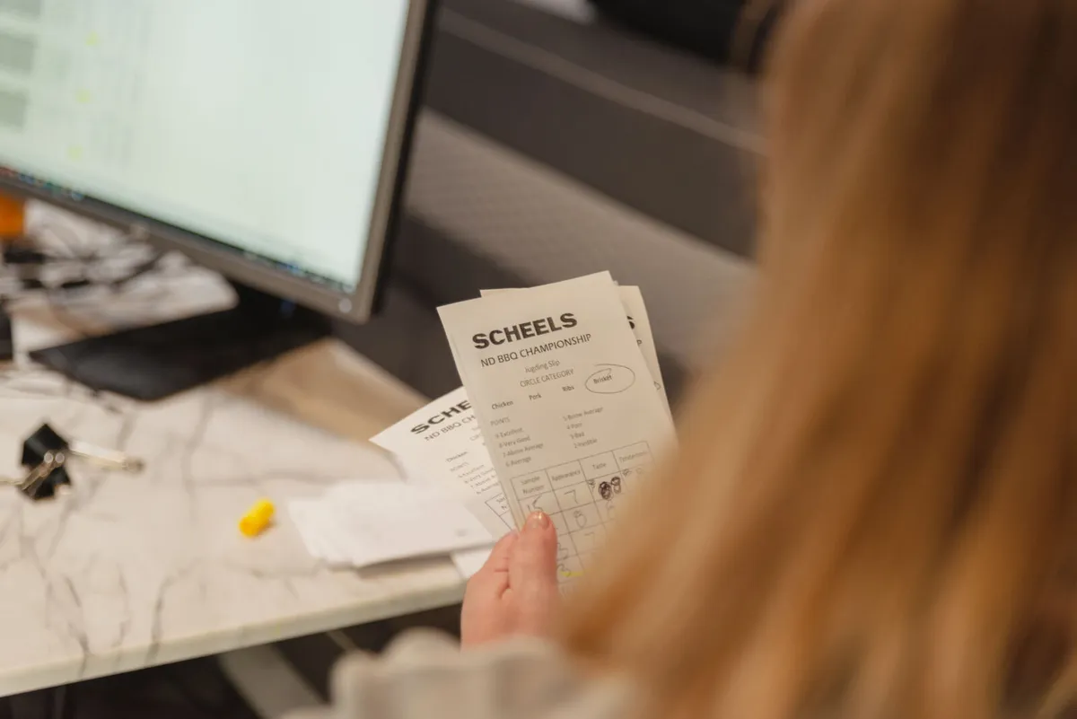 Person reviewing Scheels ND BBQ Championship judging scoresheets at a desk