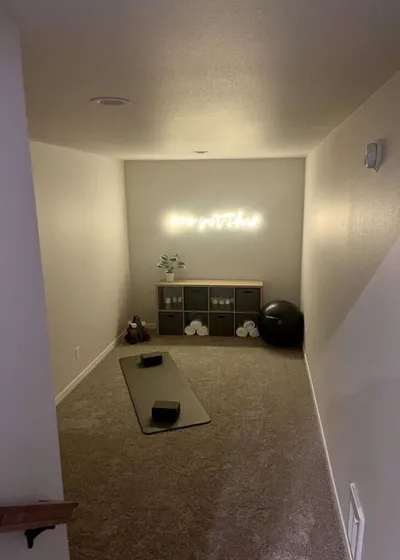 Home yoga room with a mat, storage shelf, and glowing neon sign on the wall