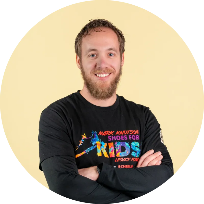 Smiling bearded man with arms crossed wearing a Mark Knutson Shoes for Kids black shirt