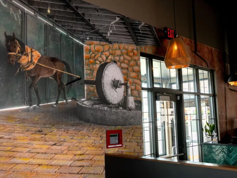 Large wall mural of a donkey turning a stone grinding wheel inside a restaurant interior