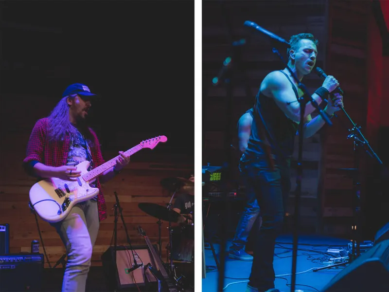 Guitarist in plaid shirt and cap performs alongside a vocalist singing into a mic stand on a dimly lit stage