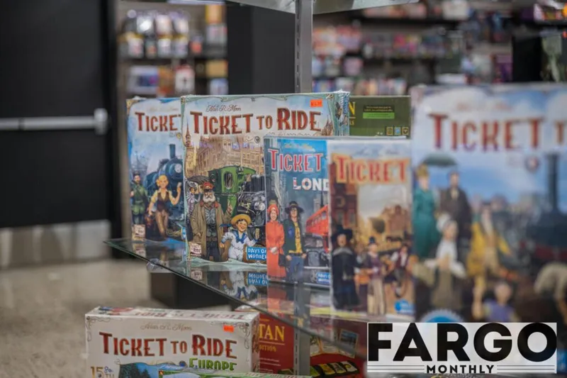 Multiple Ticket to Ride board game editions displayed on a glass shelf in a game store