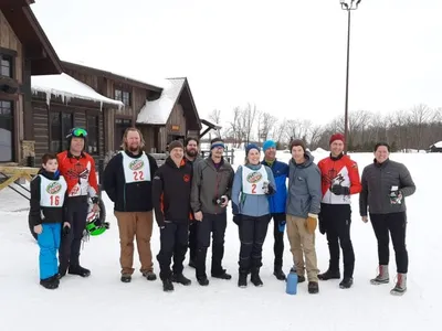 Group of about ten people in winter gear posing outside a ski lodge in snowy conditions