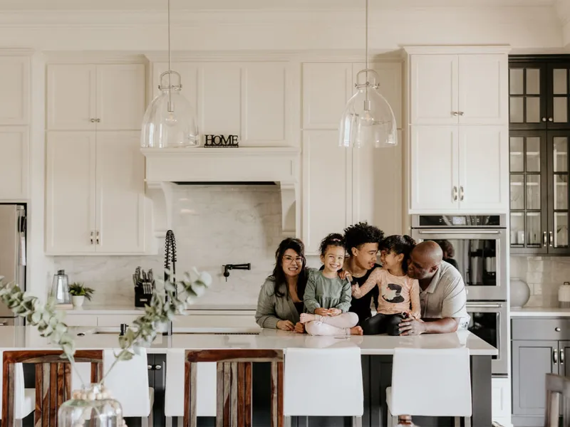 Family of five laughing together around a white kitchen island in a bright modern kitchen