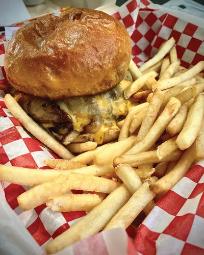 Cheeseburger with melted cheese and caramelized onions on a brioche bun, served with crispy fries in a red checkered basket