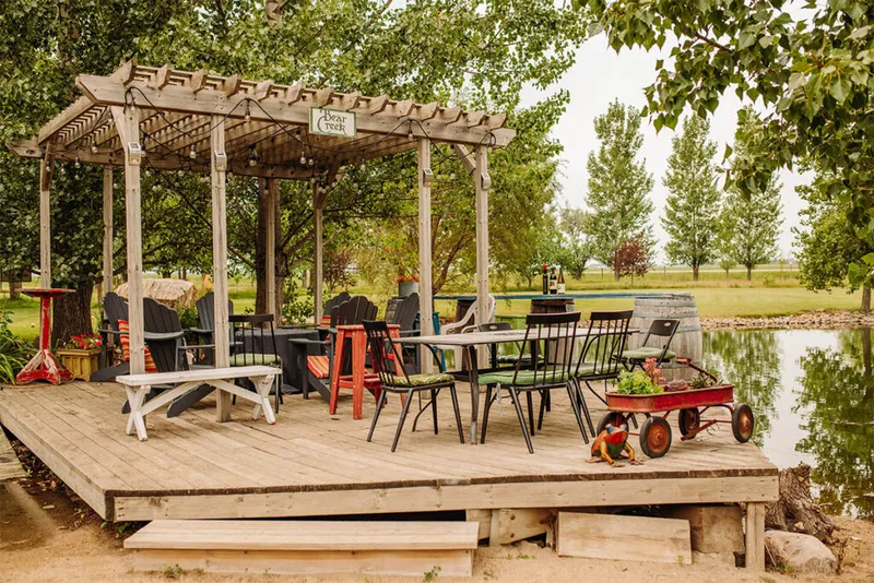 Rustic wood deck with pergola, mixed seating, and a wine barrel beside a calm pond