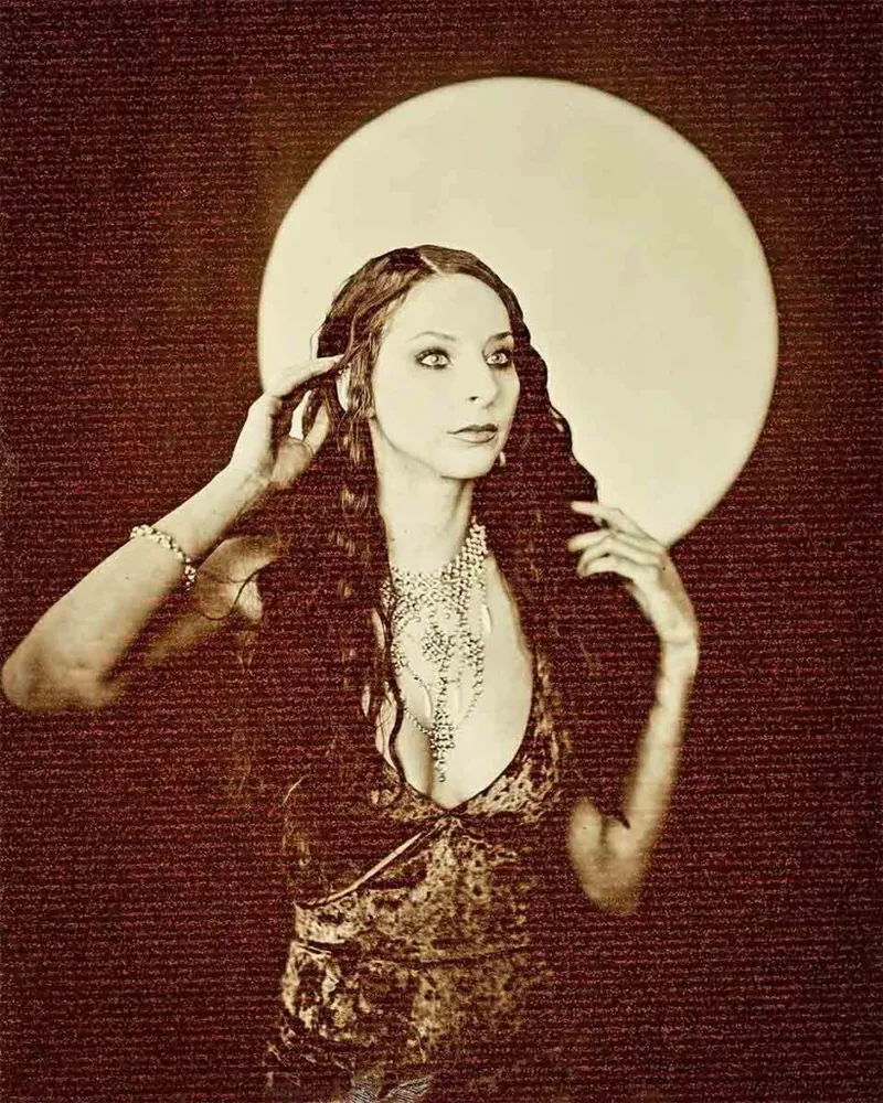 Woman with long wavy hair poses in sepia-toned wet plate portrait with large circular orb behind her