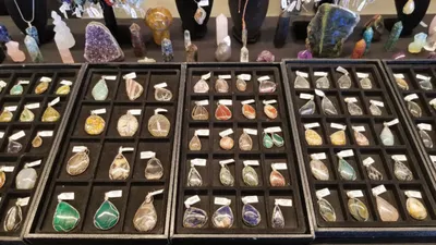 Rows of colorful gemstone pendants displayed in black trays at a market booth