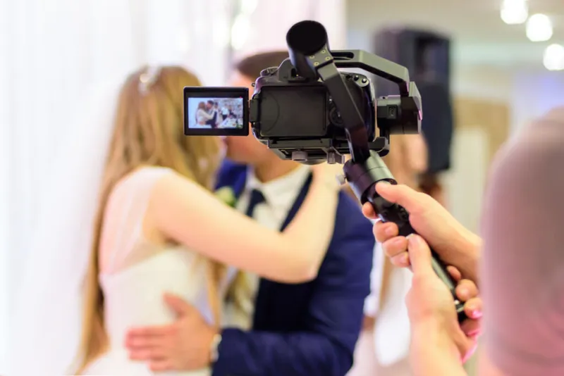 videographer holding their video camera recording a married couple kissing on their wedding day