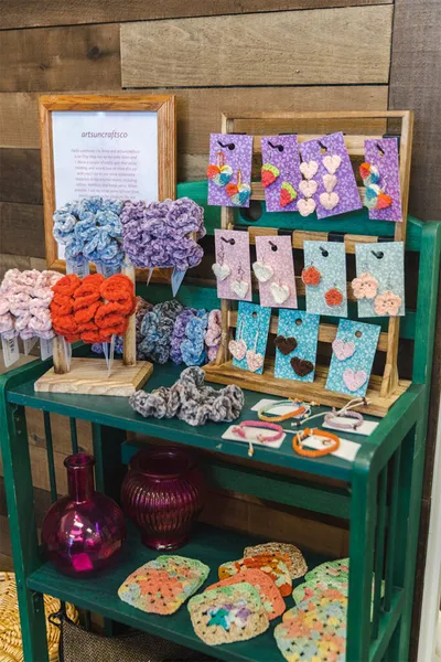 Green shelving display with colorful crochet scrunchies and handmade earrings on card backers
