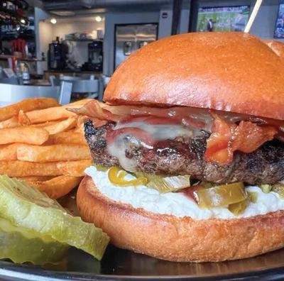 Loaded burger with bacon, melted cheese, and lettuce on a brioche bun, served with crinkle-cut fries