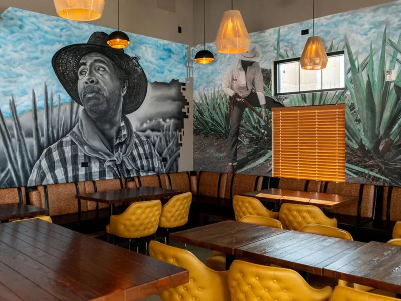 Restaurant dining room with agave mural and yellow tufted chairs around wood tables